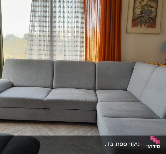 ספה אפורה גדולה בסלון מואר עם וילונות כתומים